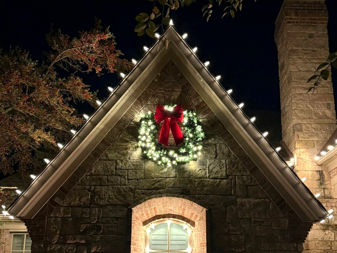 Stone gable with roofline lights and a lit wreath with a red bow