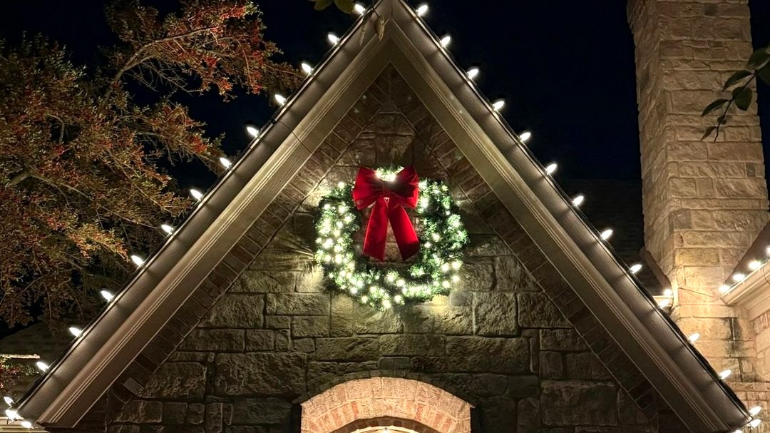 Stone gable with roofline lights and a lit wreath with a red bow