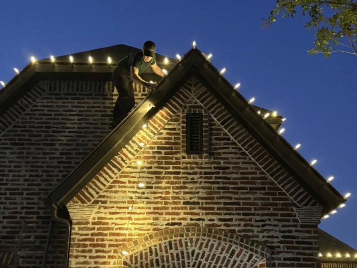 Bright's crew member installing roofline lights on a brick gable