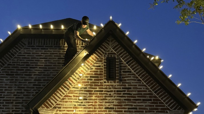 Bright's crew member installing roofline lights on a brick gable