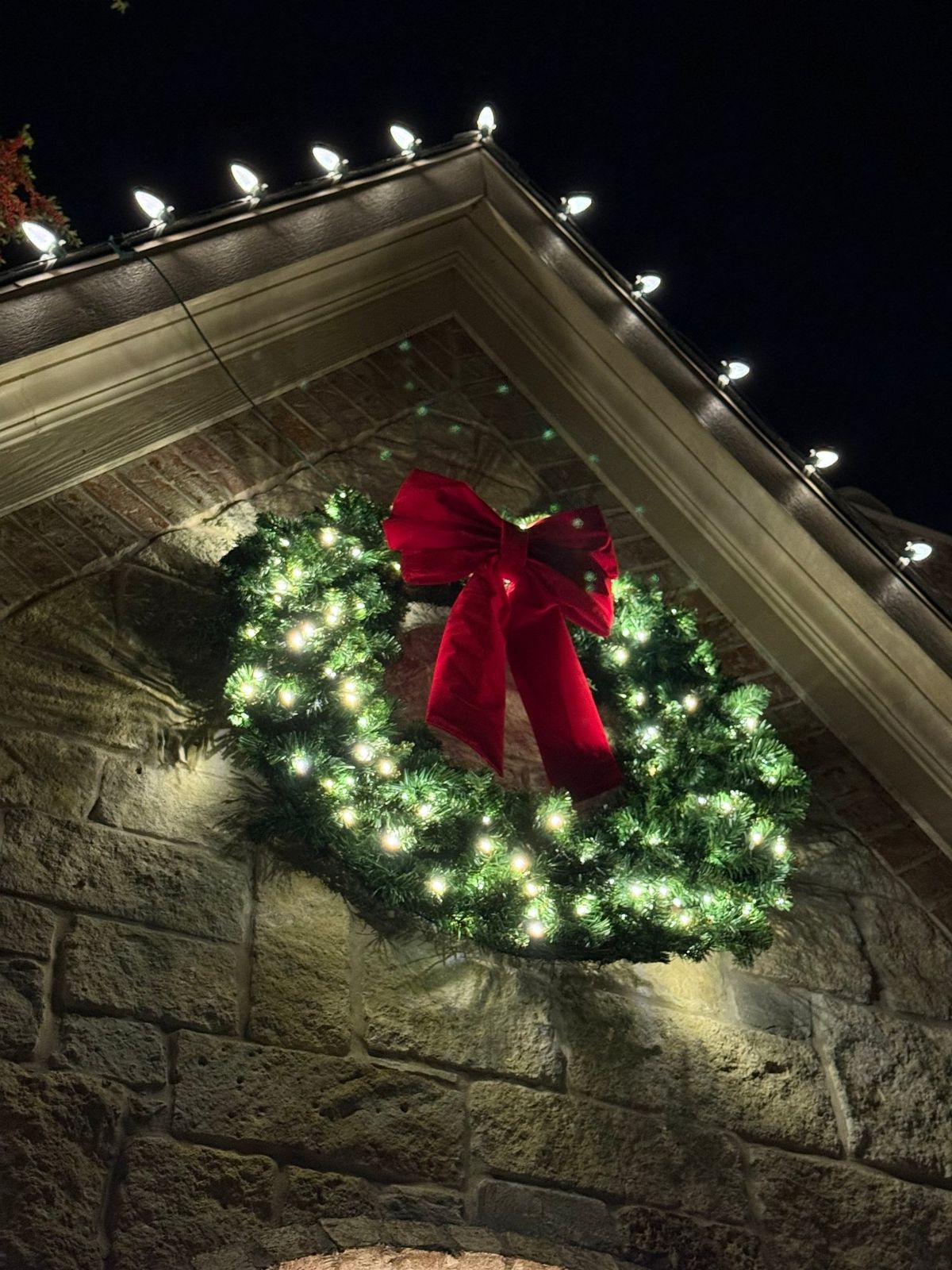 Lit wreath with a red bow under a roof peak
